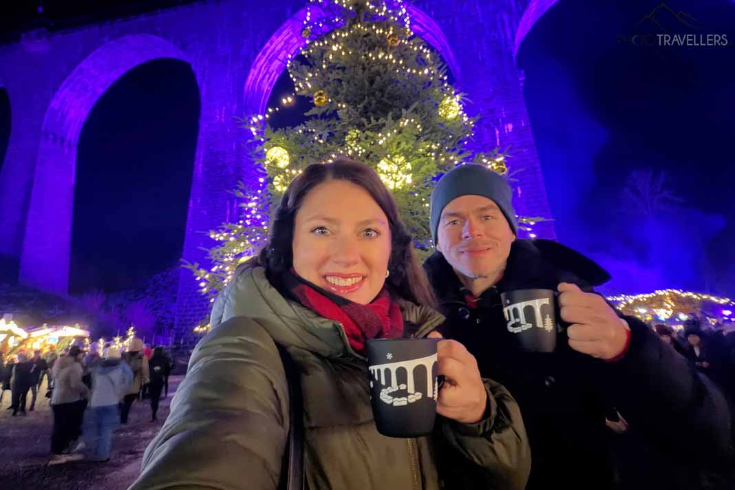 Die Reiseblogger Biggi Bauer und Florian Westermann mit einer Tasse Glühwein auf dem Weihnachtsmarkt in der Ravennaschlucht