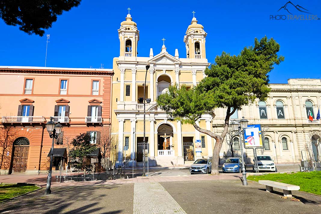 Eine Kirche mit zwei Türmen wird flankiert von dreistöckigen Gebäuden in einem Park in Taranto