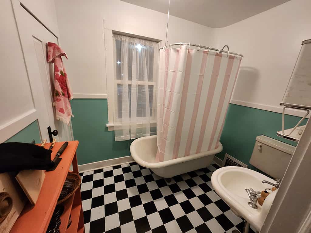 bathroom-1 Vintage bathroom with clawfoot tub, pink-striped shower curtain, black and white checkered floor, and retro fixtures.