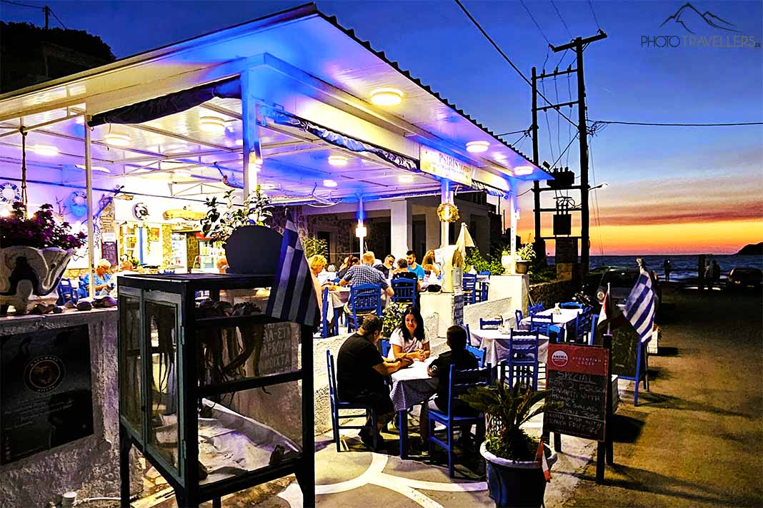 Menschen sitzen im Abendrot an den Tischen einer Taverne in Kantouni