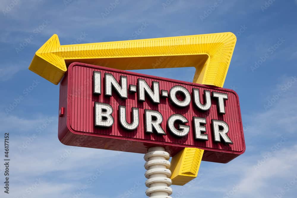 A classic IN-N-OUT BURGER sign in front of sky with yellow arrow