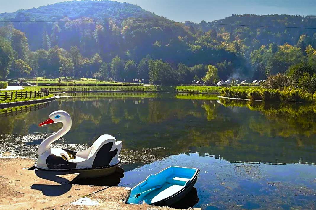 Ein kleines Boot und daneben ein als Schwan dekoriertes Boot dümpeln am Steg in Abenteuerpark in Brasov