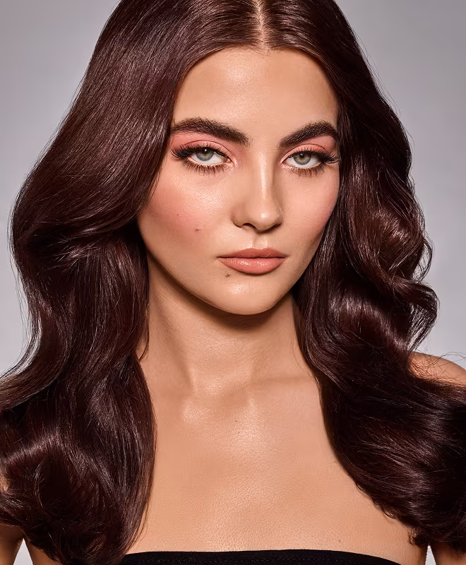 Porträt einer Person mit langen, glatten, kastanienbraunen Haaren und sanften Makeup-Tönen.