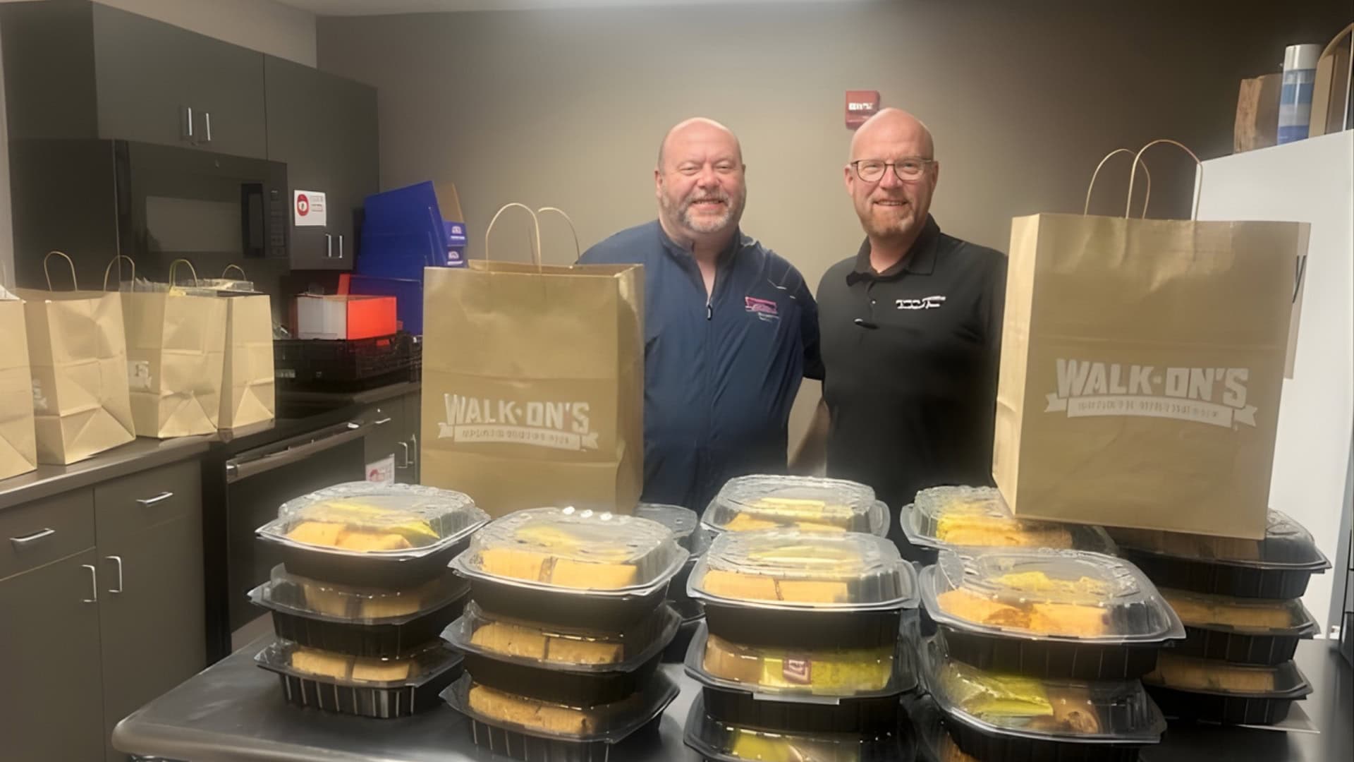 Two Walk-On’s team members with stacks of packaged holiday meals and branded bags