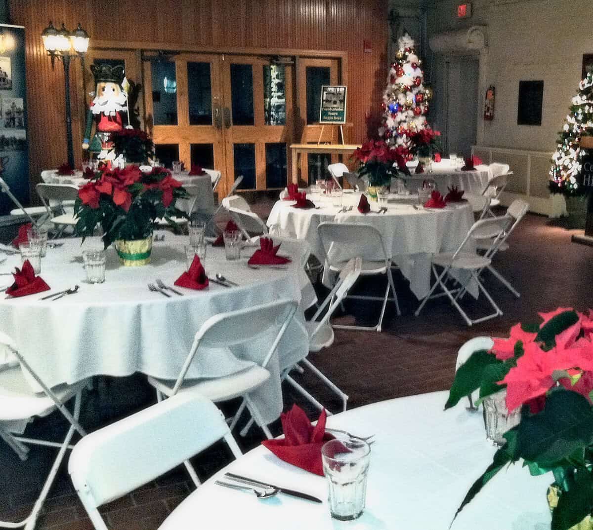 Carriage House at Christmas_retouch Festive holiday event setup at The History Museum with decorated tables, poinsettias, Christmas trees, and seasonal decor for a museum holiday celebration.