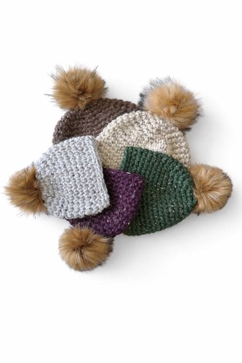 Five beanies with faux fur pom-poms in brown, cream, gray, purple, and green form a circle on a white background. Free crochet pattern