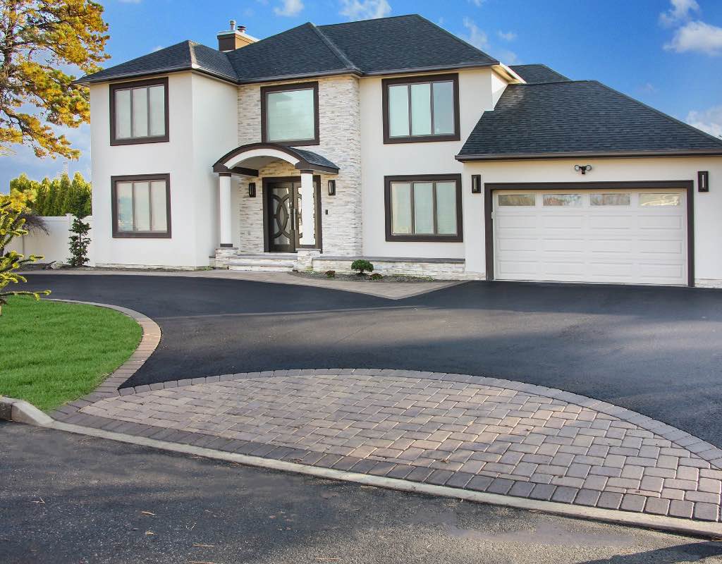 Modern two-story house with white and stone facade, double garage, and curved driveway.