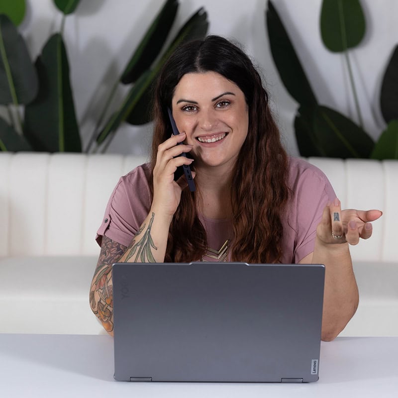 A marketing agency professional smiles while talking on the phone and working on a laptop.