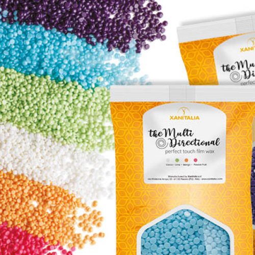 Zakjes ontharingswaxkorrels van Xanitalia in diverse kleuren, met uitgestrooide waxparels op de achtergrond.