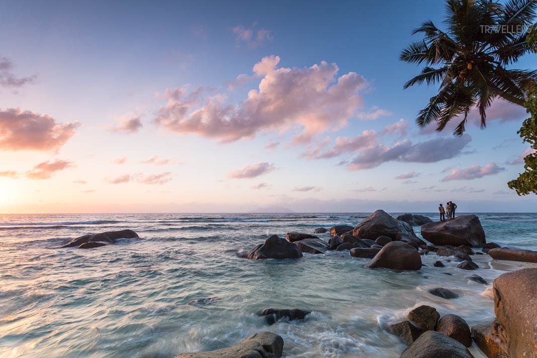 Der Strand Beau Vallon auf Mahé im Licht der Abenddämmerung. Rechts ragt eine Palme in das Bild