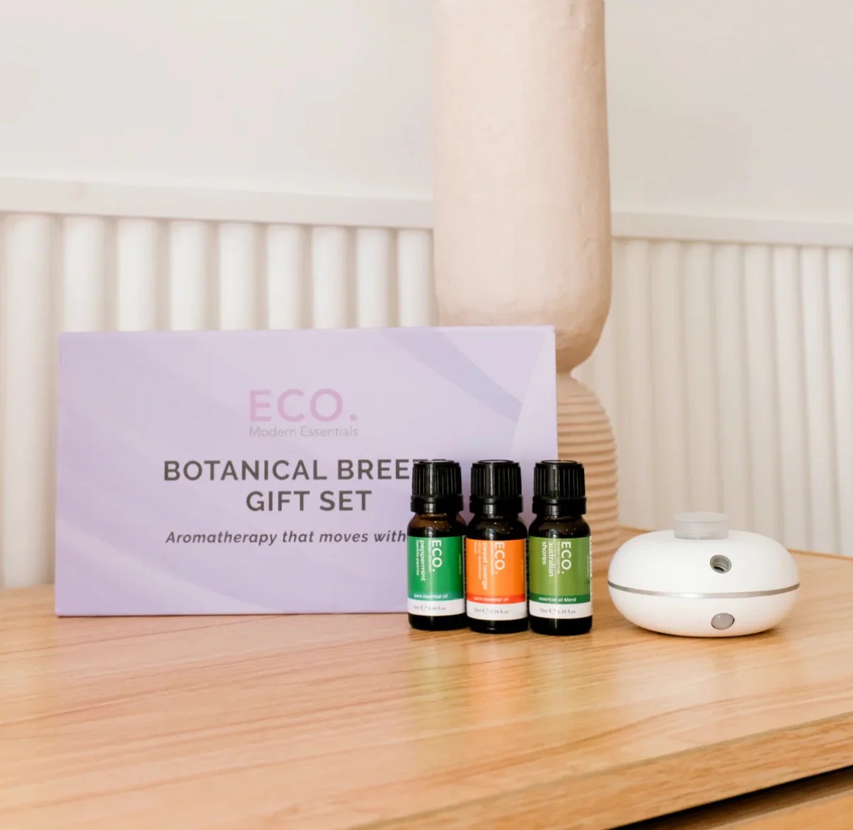 Revive & Thrive Aromatherapy Bundle 1 The Botanical Breeze Gift Set features a motion sensor diffuser and three essential oils, elegantly displayed on a wooden surface in a softly lit room.