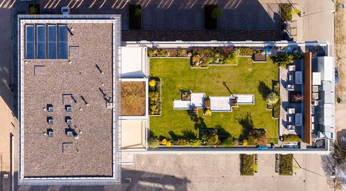 Luftaufnahme eines rechteckigen Gartens mit Rasenfläche, Beeten und Gartenmöbeln, umgeben von weißen Zäunen.
