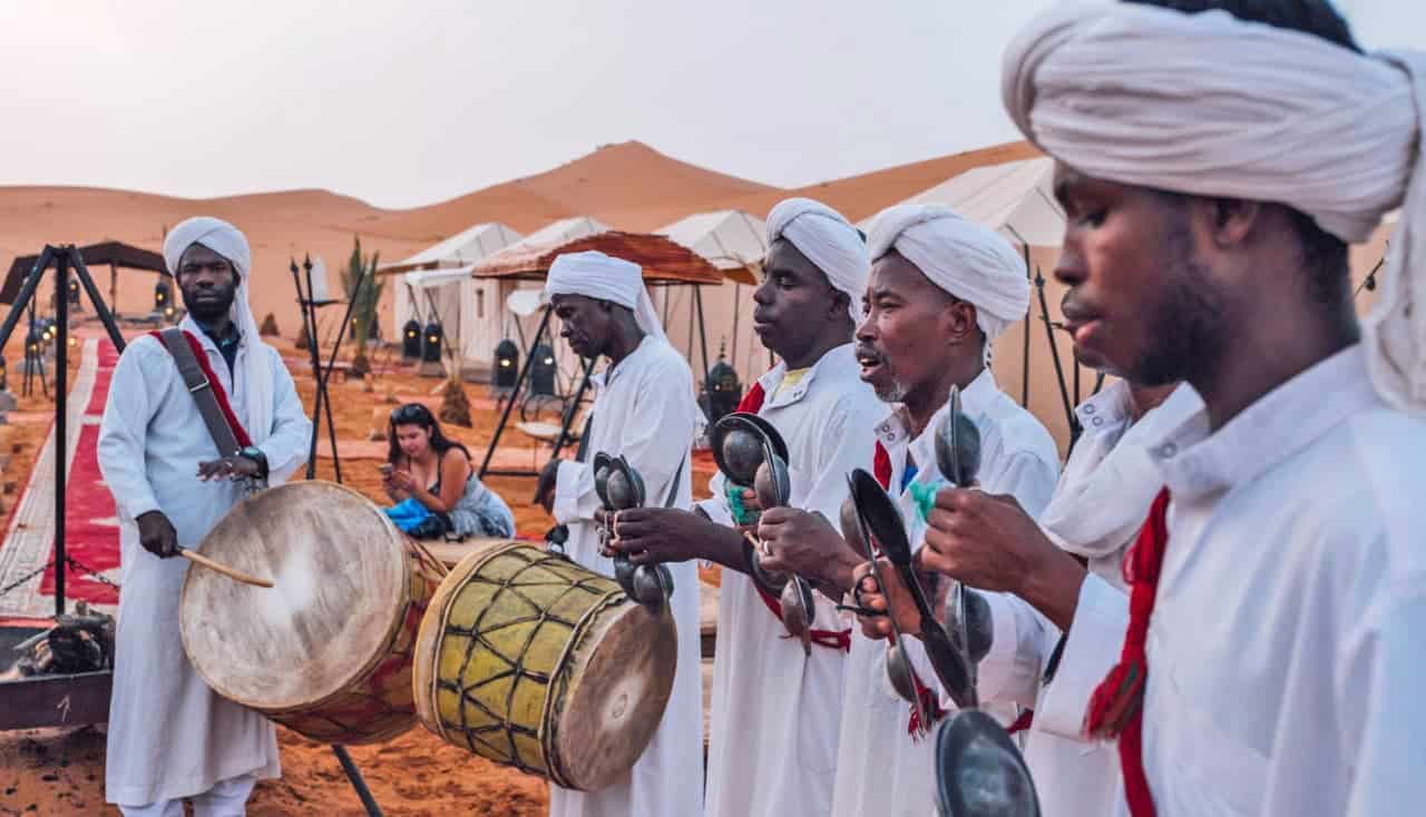 Músicos en el desierto de Marruecos tocando tambores tradicionales en un entorno arenoso.