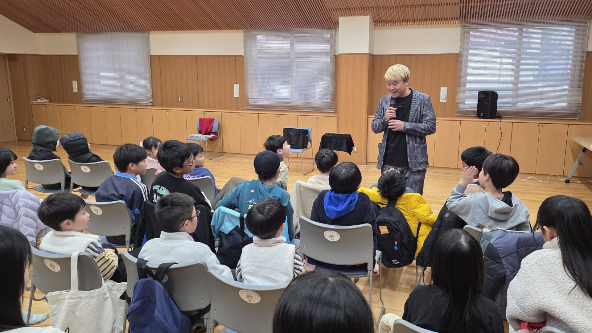 富山市の児童クラブでクリスマス会!大人も子供も一緒に楽しむマジックショー 1 マイクを持って子供たちに語りかけるコンプレッサー。富山市のクリスマス会イベントで、マジシャンと子供たちが一体となって楽しんでいる様子