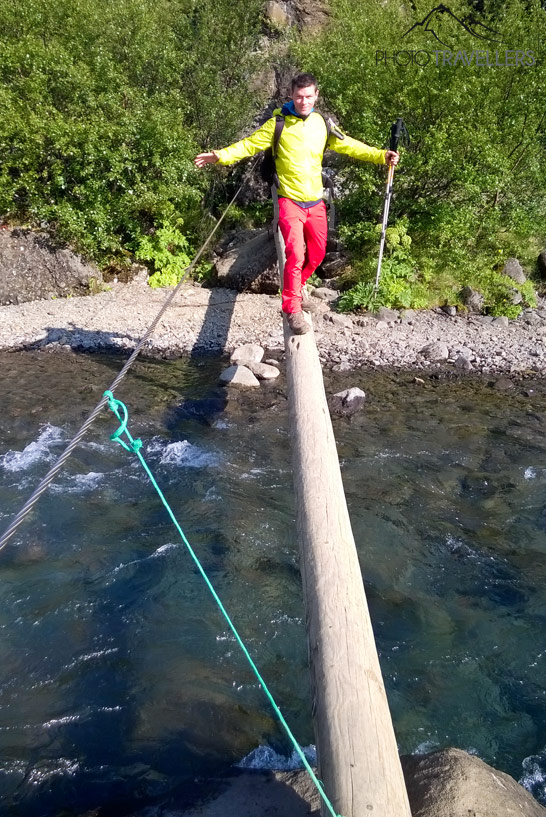 Reiseblogger Florian Westermann balanciert auf einem Baumstamm über dem Fluss Botnsá in Island