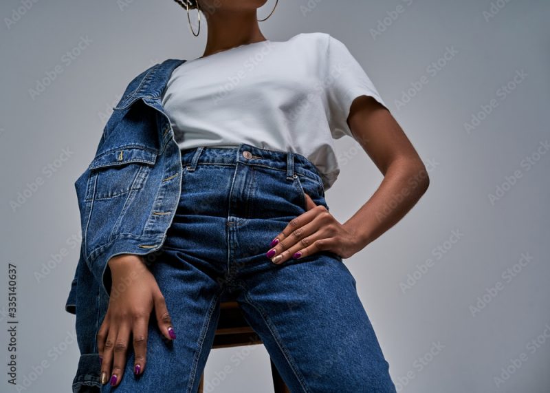 Girl in white t-shirt in jeans with denim jacket posing on camera holds hands on hips. Fashion concept
