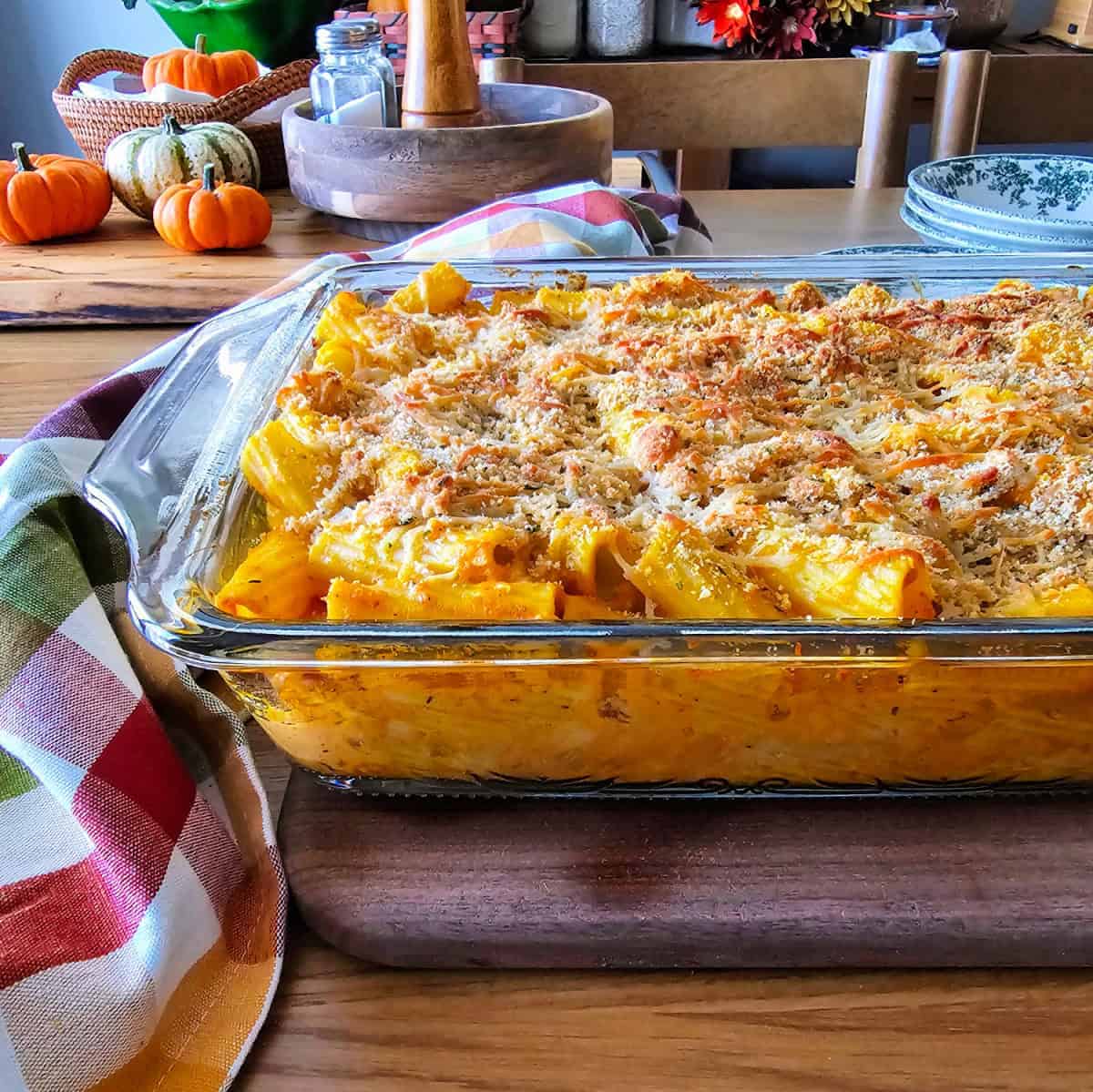 A pan of creamy pumpkin and sausage baked rigatoni with fall decorations in the background.