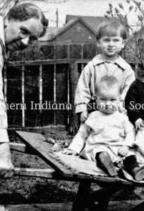 children in a wheelbarrow c. 1920s 1930s ph YPOH Szymanski (1) Childhood outdoor playing with woman and kids in backyard, vintage black and white photo.