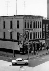 A LOOK BACK - 1960s Main Street ph 1897 Old downtown building with Main Hotel, radio station and storefronts, vintage cars, and pedestrians.