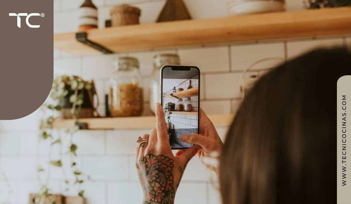 Persona sosteniendo un celular y explorando imágenes de cocinas integrales modernas en la pantalla, en busca de ideas para diseñar su espacio.
