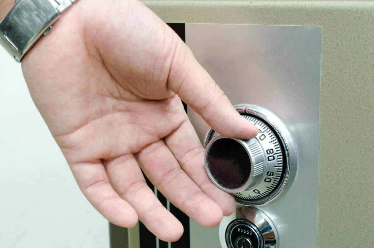 A close-up image of a hand wearing a wristwatch, turning the dial of a combination safe. The safe, metallic and sturdy, showcases a circular combination lock with numbers visible on the dial. It’s the precise moment that would intrigue any seasoned locksmith.