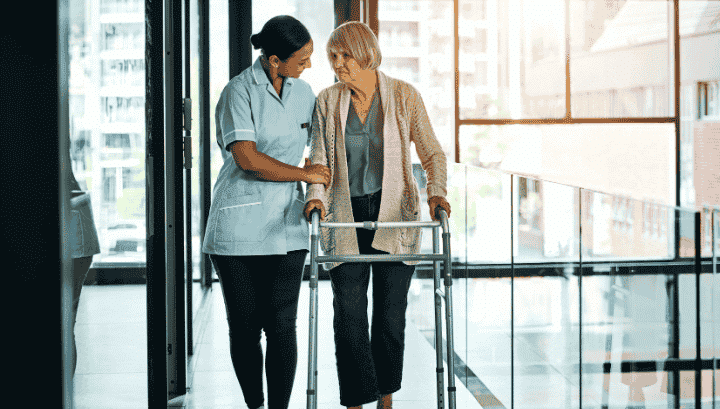 Specialized and Extended Care for Seniors | Professional Elderly Support Services.png Caregiver assisting a senior woman with a walker, symbolizing specialized and extended care services, including elderly care and daily living assistance.