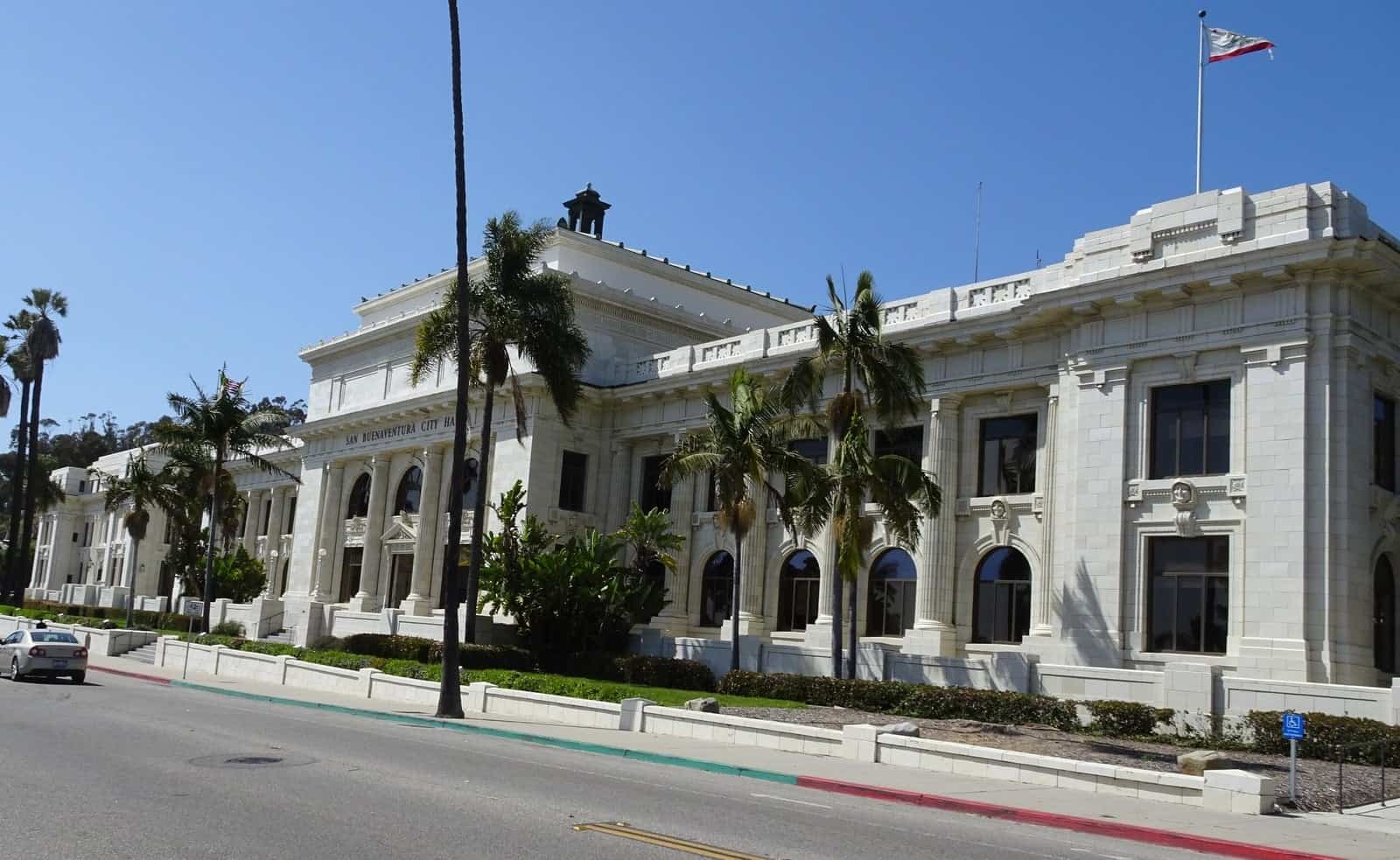 Ventura City Hall, a white neoclassical building with a copper dome and columns, on a hillside above a palm-lined street.