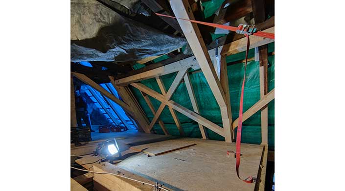 Dachboden mit sichtbaren Holzbalken, grüne Plane und Bauenmaterialien, teilweise abgedeckt mit Staub und Schmutz.