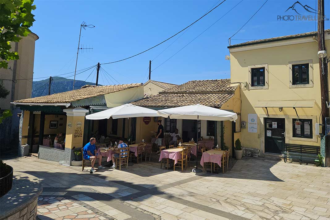 Gästen sitzen an den Tischen einer kleinen Taverne unter Sonnenschirmen