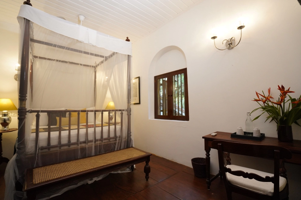 The Lime Butterfly room in Adigar's Manor, showcasing a canopy bed and a table in a serene bedroom setting.