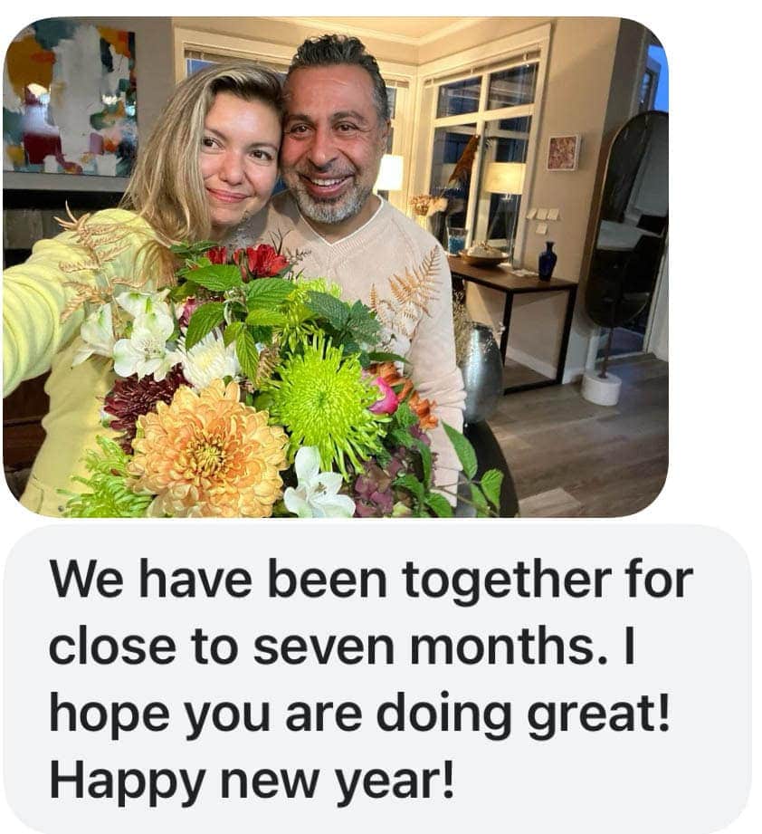 A smiling couple poses indoors, holding a large bouquet of flowers. A cheerful New Years message is written below the photo: "We have been together for close to seven months. Happy New Year!"