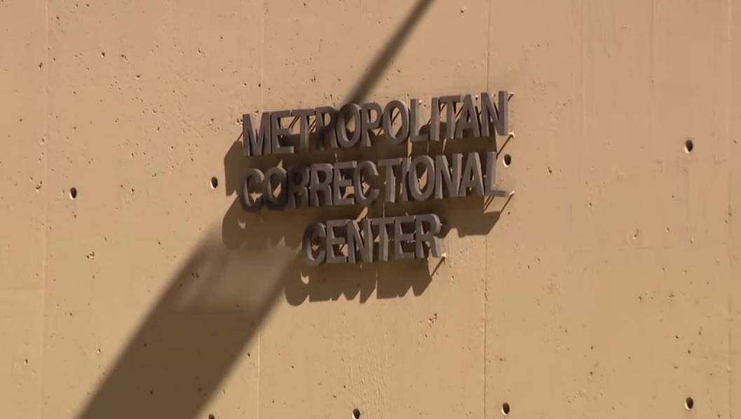 The sign for the Metropolitan Correctional Center, a Chicago prison, is visible on a tan wall. The sign's metallic letters cast a shadow, hinting at the potential for prison abuse within the facility, as seen in the Brittany Hall inmate abuse case and the Heather Mack prison charges.