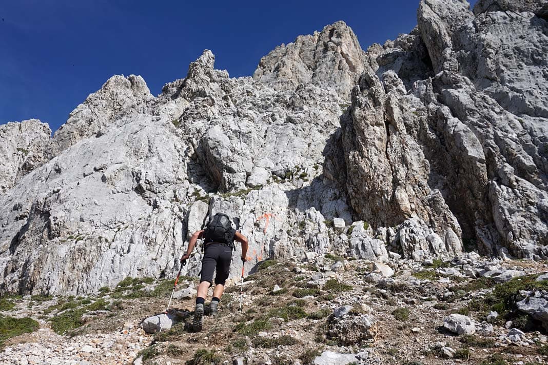 Ein roter Pfeil an einer Felswand, der den Einstieg in eine Rinne auf der Hochwanner-Wanderung anzeigt. Davor ein Wanderer
