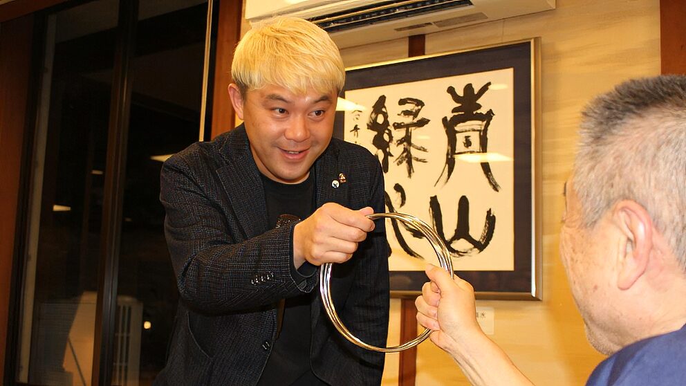 神通峡の絶景に癒されて!太極拳の皆さんと楽しむマジックショー in 楽今日館 2 マジシャン・コンプレッサーが至近距離で披露する、チャイナリングのクロースアップマジック。大きなリングが重なり合う不思議な光景を、驚きを隠せないゲストのすぐ目の前で実演している様子。