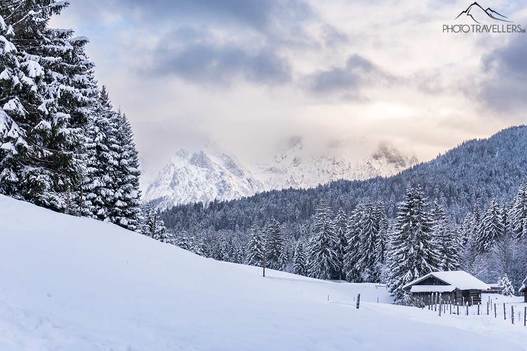 Eine verschneite Hütte im Wald mit Blick auf die Berge