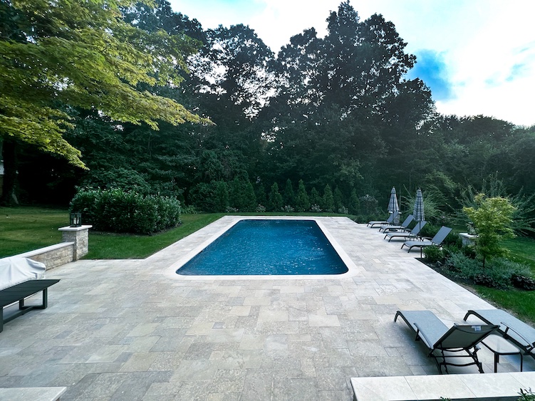 A pool with chairs and trees in the background.