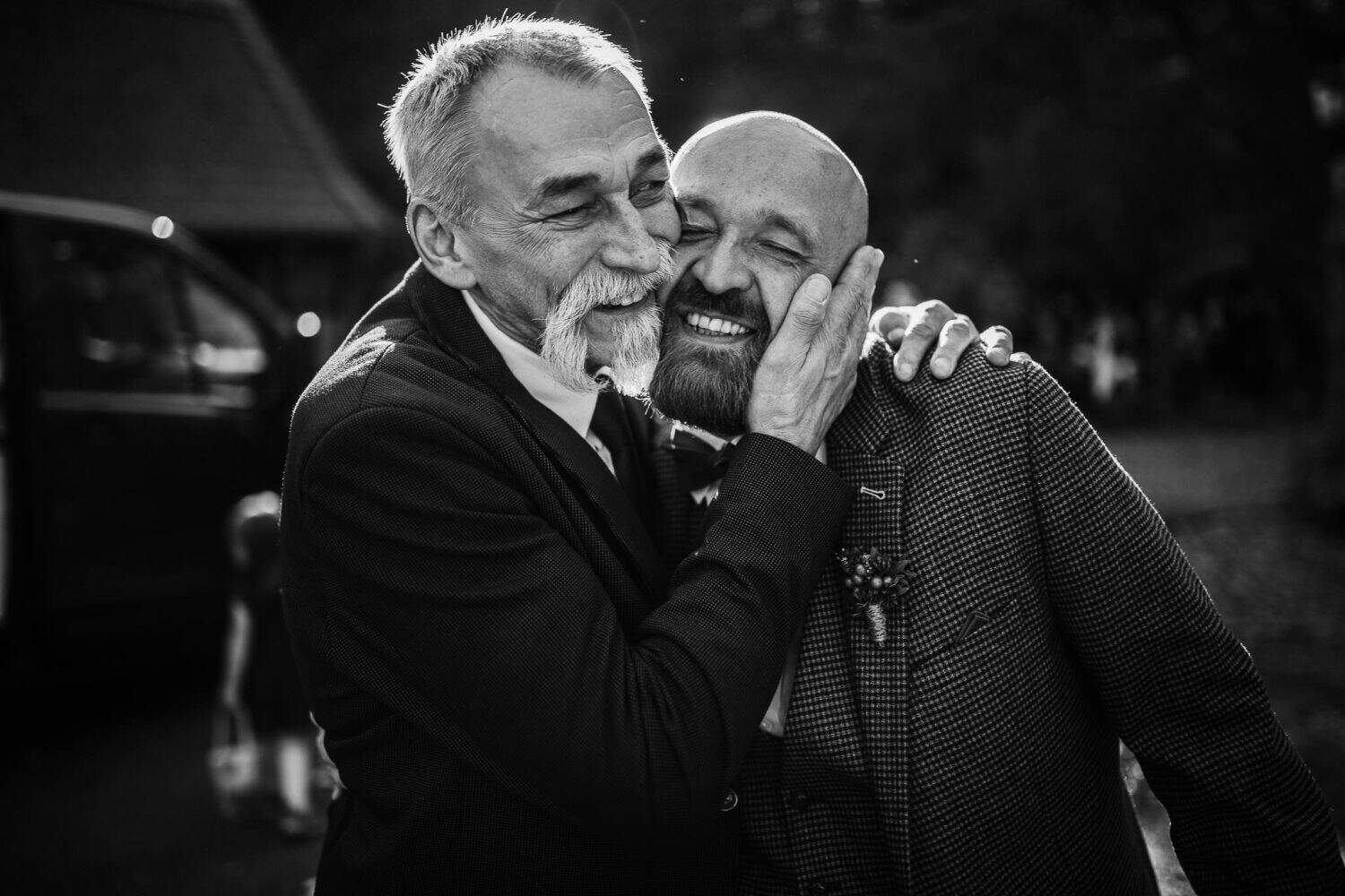 Ein Vater hält sanft das Gesicht seines Sohnes, während sie ein Lächeln teilen – Hochzeitsreportage NRW im Freien.