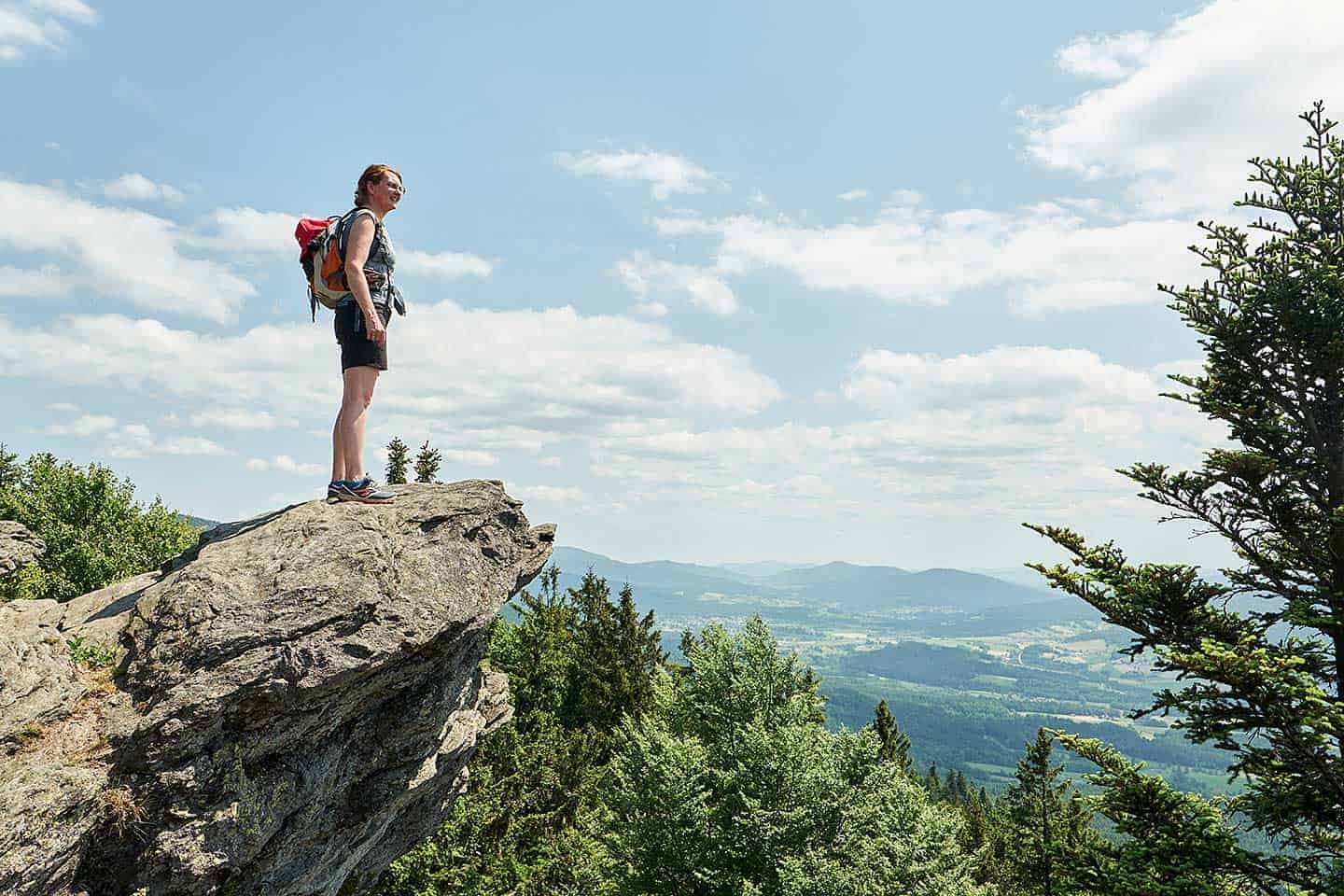 Eine Wanderin steht auf einem Aussichtspunkt im Bayerischen Wald und genießt das Panorama
