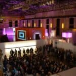 Ein Foto einer Menschenmenge bei einer Veranstaltung in der Halle. Es sind viele verschiedene Stände aufgestellt.