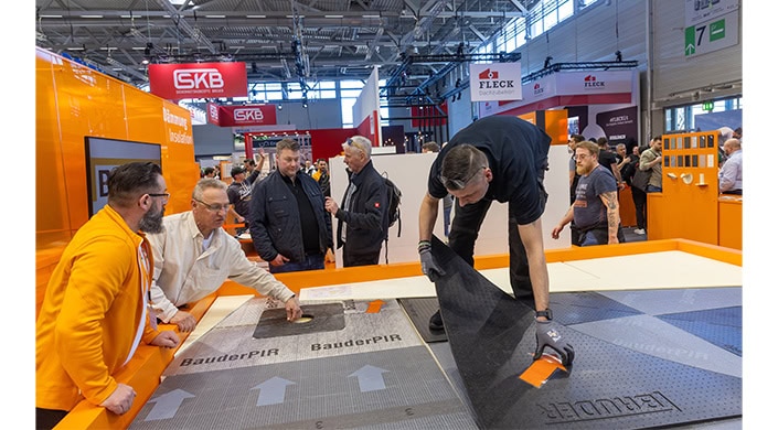 Mehrere Männer stehen auf einer Messe, während einer eine Platte mit der Aufschrift "BauderPIR" bearbeitet.