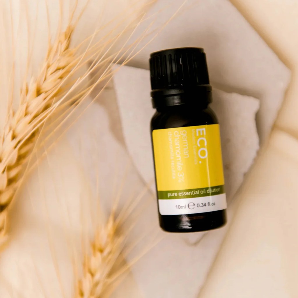 A 10ml bottle of German Chamomile 3% in Grapeseed Oil sits on a white stone, encircled by wheat stalks against a beige backdrop.