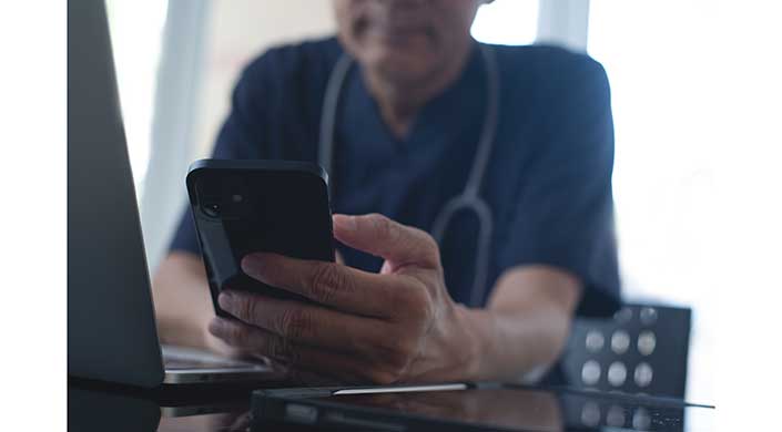 Eine Person hält ein Smartphone in der Hand und blickt darauf, unscharfer Hintergrund.