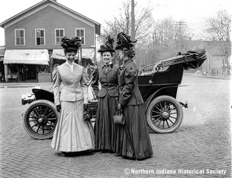 3 ladies car Women in early 20th century fashion standing in front of a vintage car outside the History Museum.