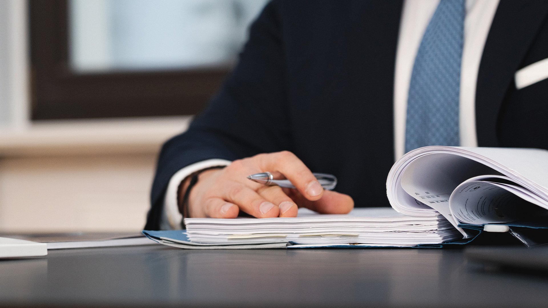 Bild von einem aufgeklappten Ordner, darauf eine Hand mit Kugelschreiber