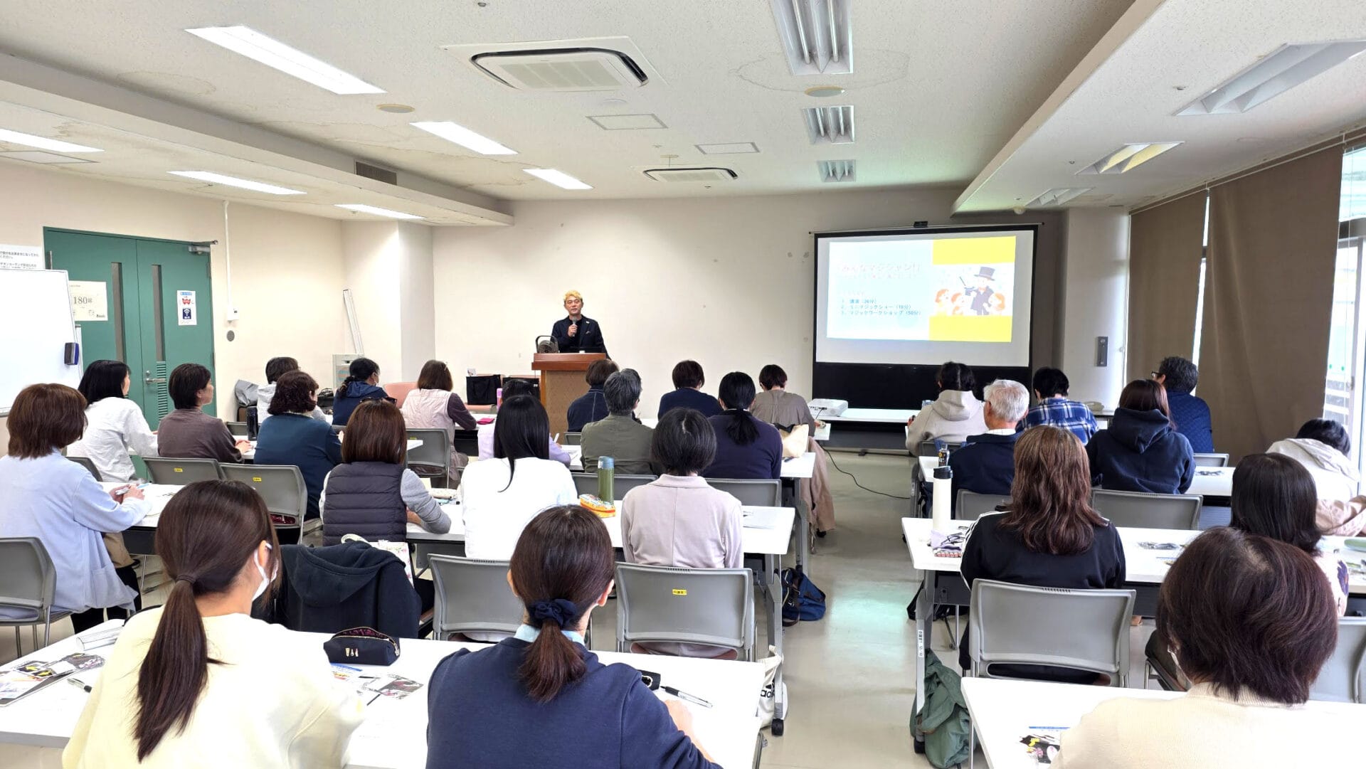 富山県の放課後児童支援員研修会に登壇。マジシャンが伝えたかった「子どもたちと心を通わせる」3つの柱 1 研修会で講演するマジシャン・コンプレッサー。会場後方からの写真で、多くの受講者が講師の話を熱心に聞いている。