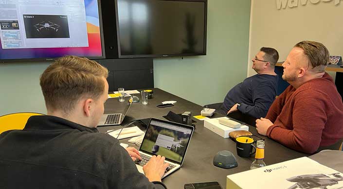 Person arbeitet an einem Laptop in einem modernen Konferenzraum mit großem Bildschirm an der Wand und verschiedenen Gegenständen auf dem Tisch.