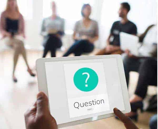 faqs for seo agency Tablet displaying question, blurred people in group discussion.