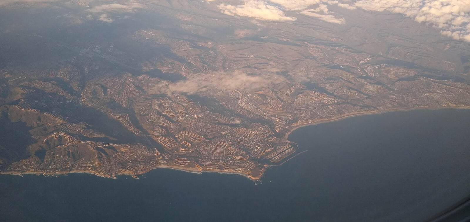 An aerial view of the Dana Point coastline in Orange County, with headlands, a harbor and hillside neighborhoods above the Pacific Ocean.