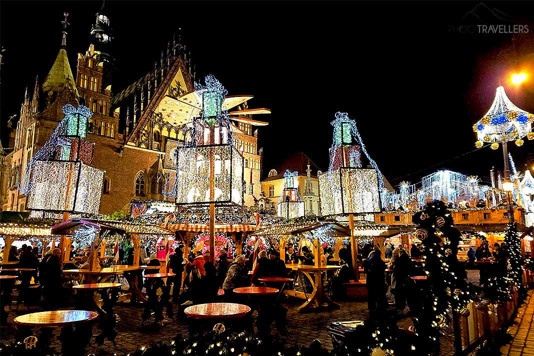 Menschen stehen an hell beleuchteten Ständen auf dem nächtlichen Breslauer Weihnachtsmarkt