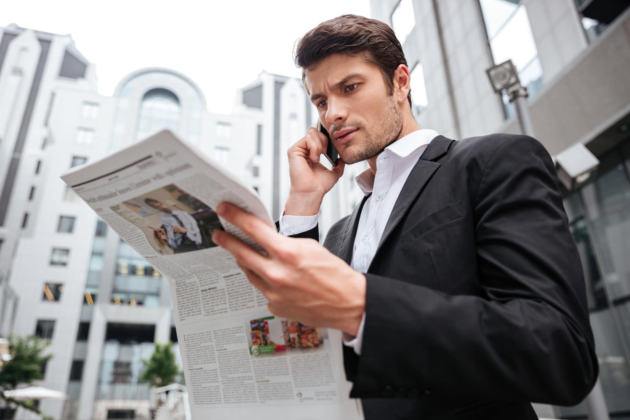 Ist eine Enteignung durch das Sanierungs- und Abwicklungsgesetz möglich? 1 concentrated young businessman talking on cell phone and reading newspaper near busine SBI 302738672